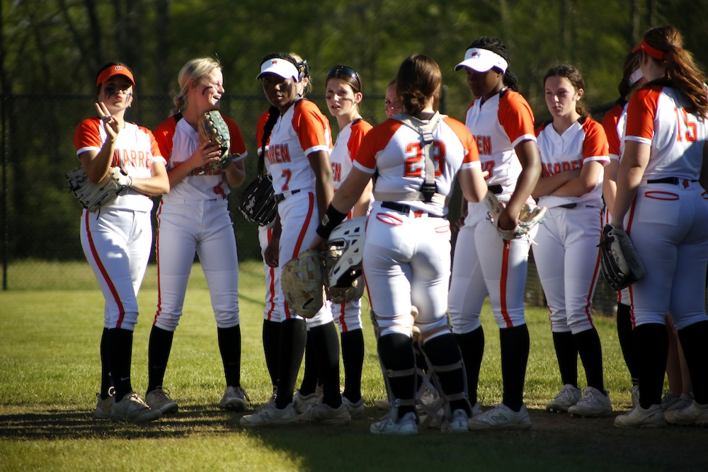 A group of women in softball uniforms standing on top of a field.