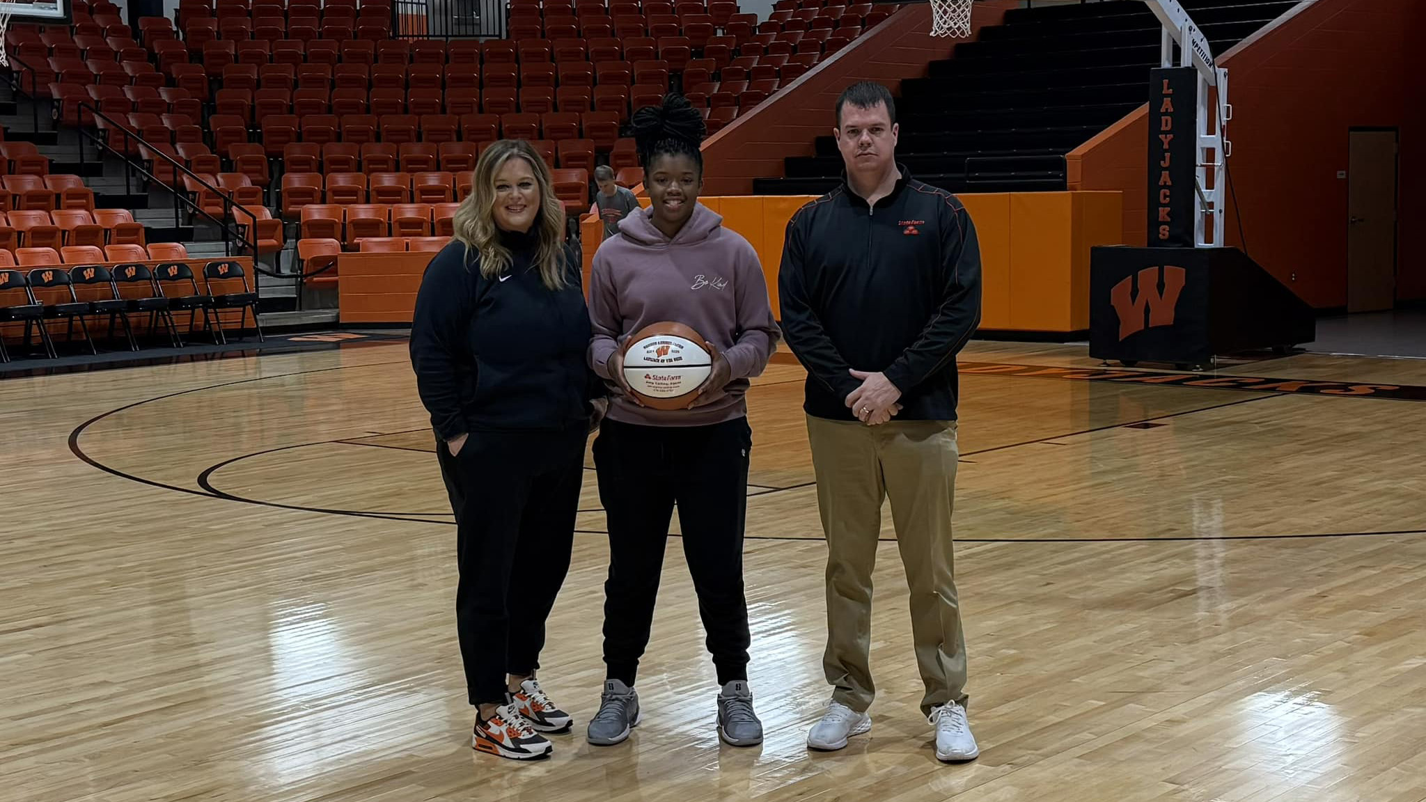 Three people standing in a gym holding a basketball.