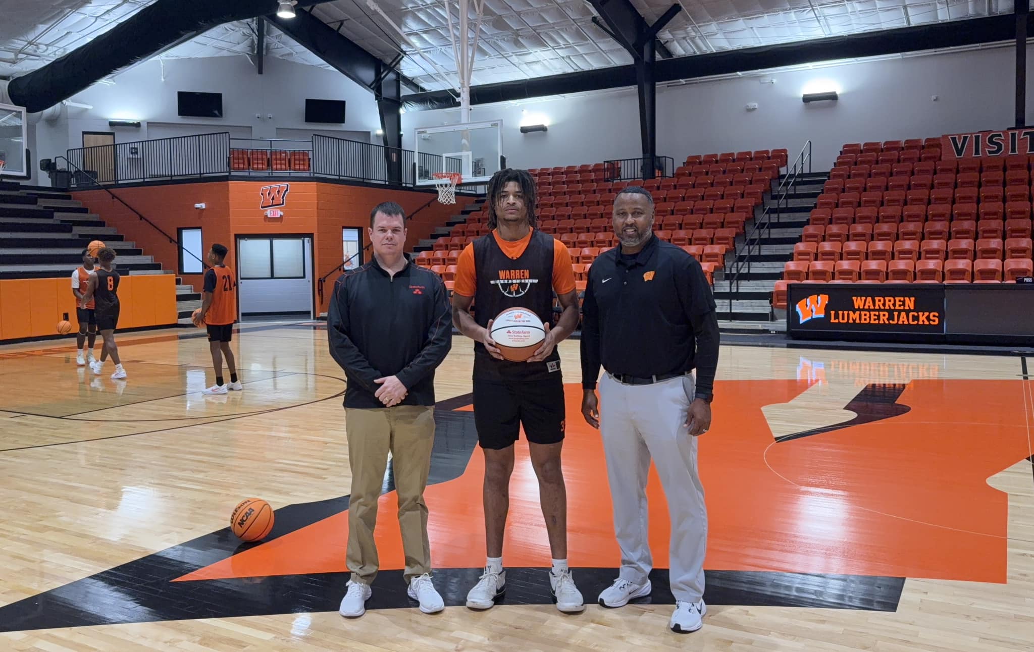 Three men standing in a gym holding a frisbee.