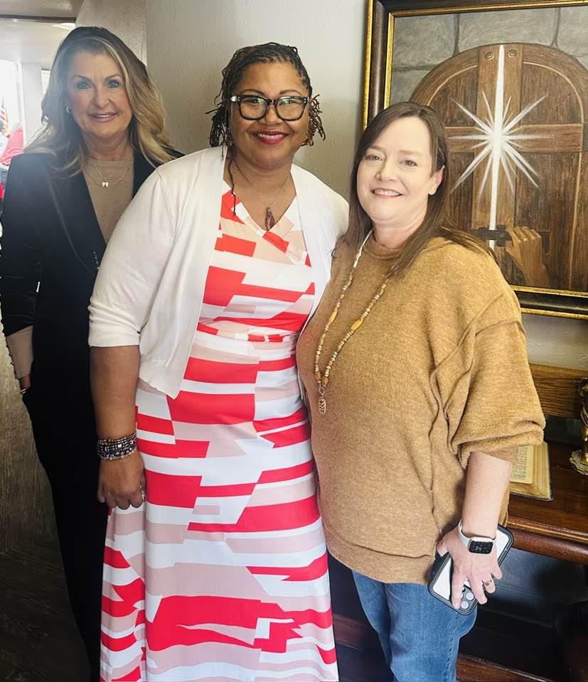 Three women standing next to each other in front of a painting.