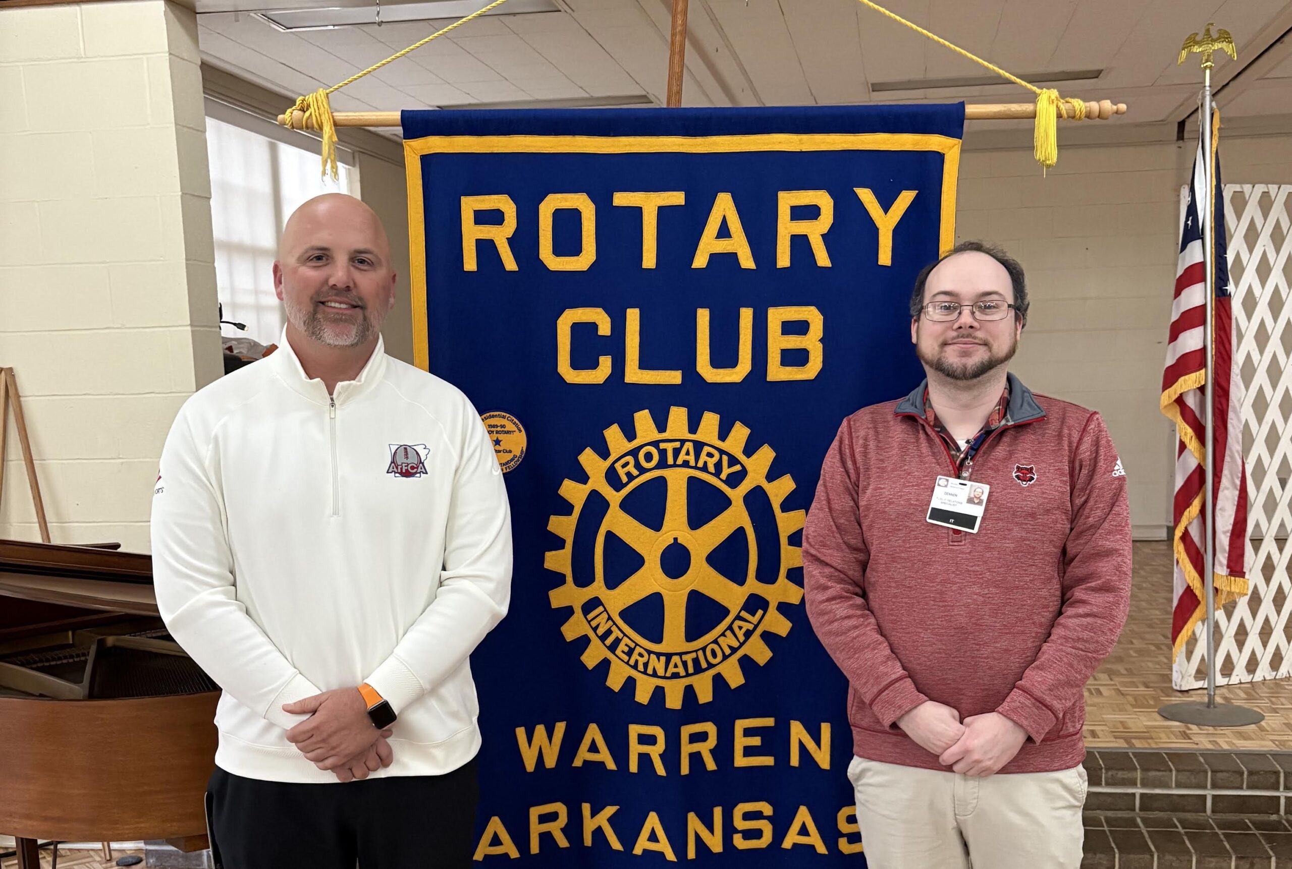Two men standing in front of a rotary club banner.