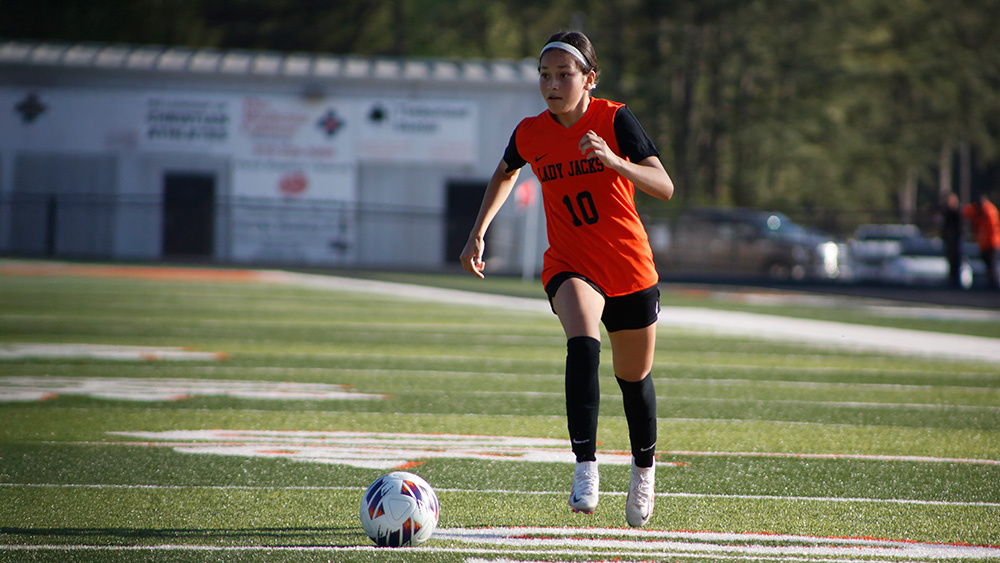 A girl in an orange shirt is playing soccer