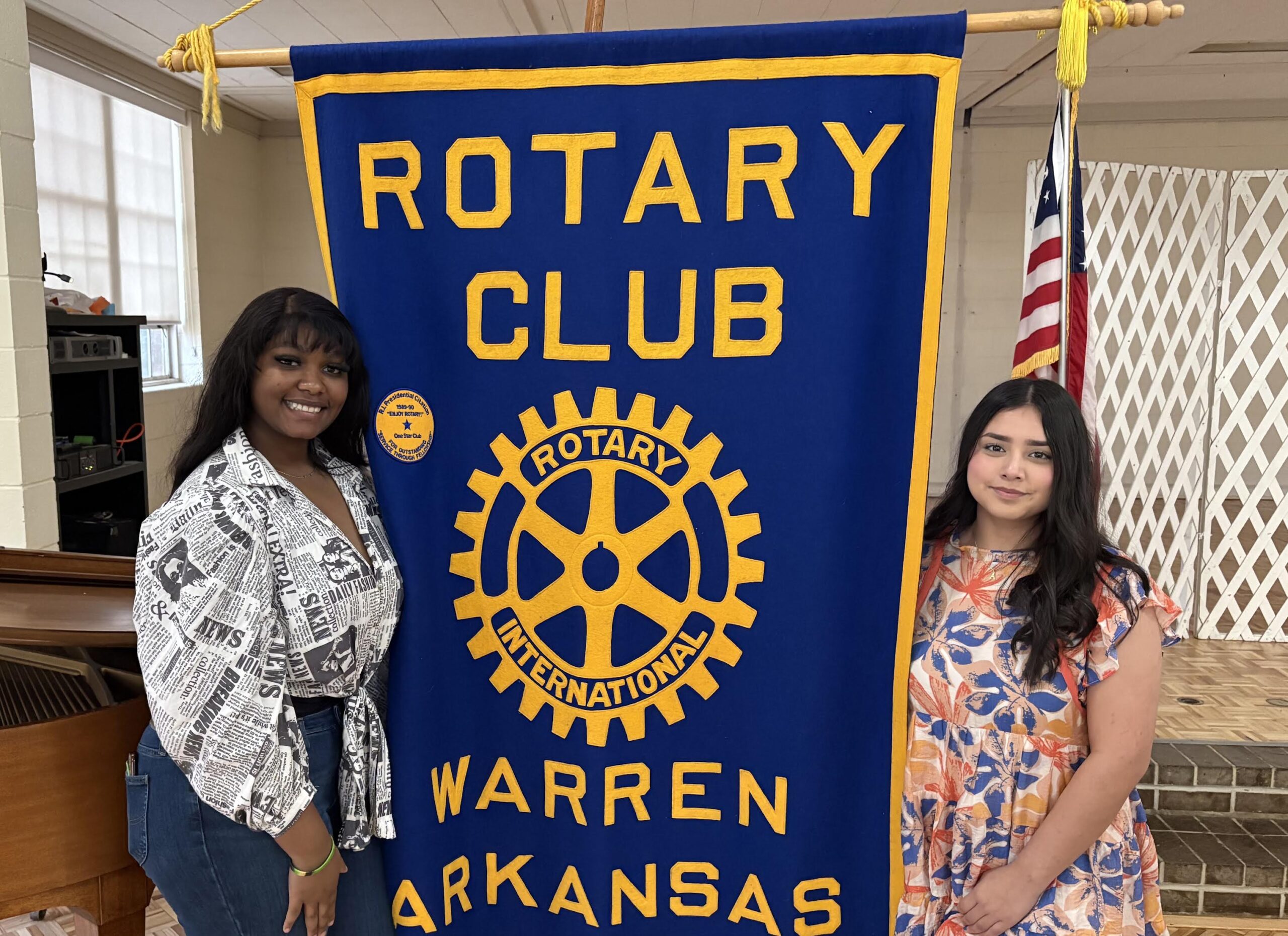 Two women standing next to a banner that says " rotary club warren arkansas ".