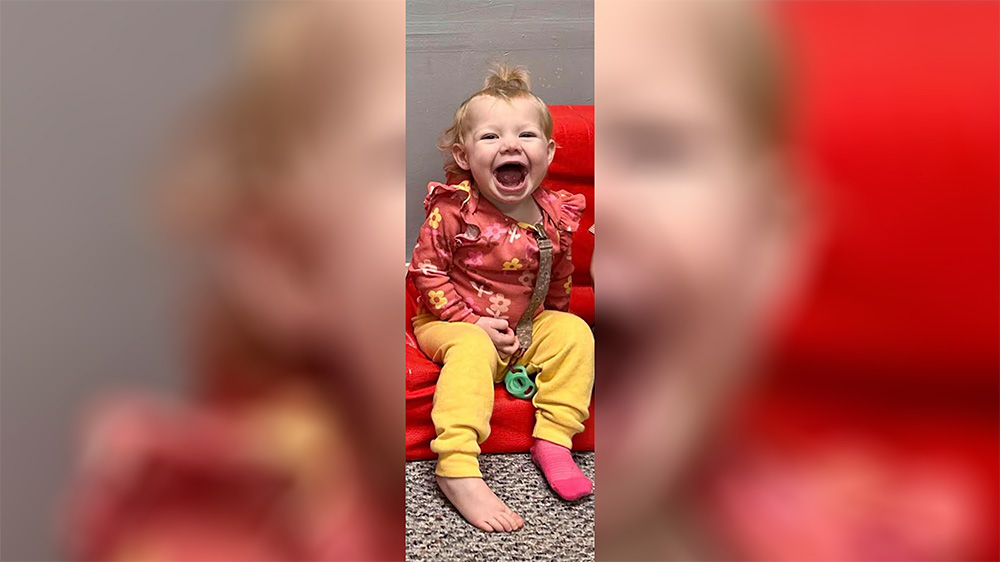 A toddler sitting on the floor laughing with his mouth open.