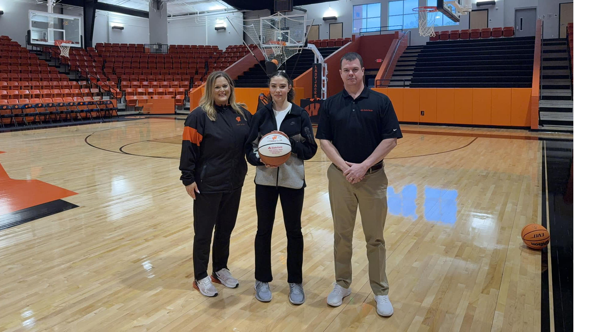 Three people standing in a gym holding a ball.