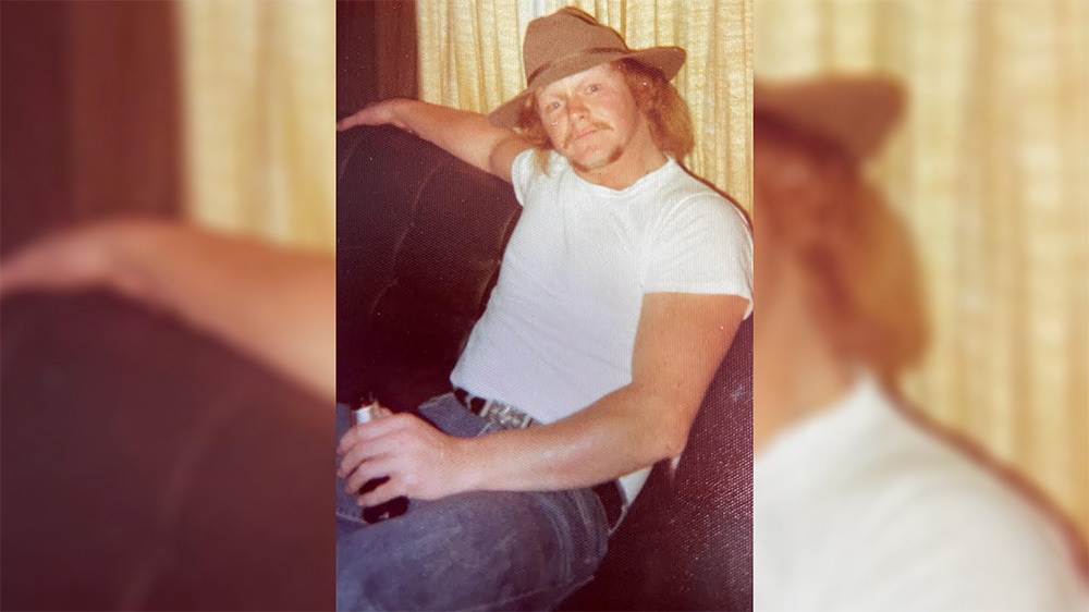 A man in white shirt and cowboy hat holding a beer.