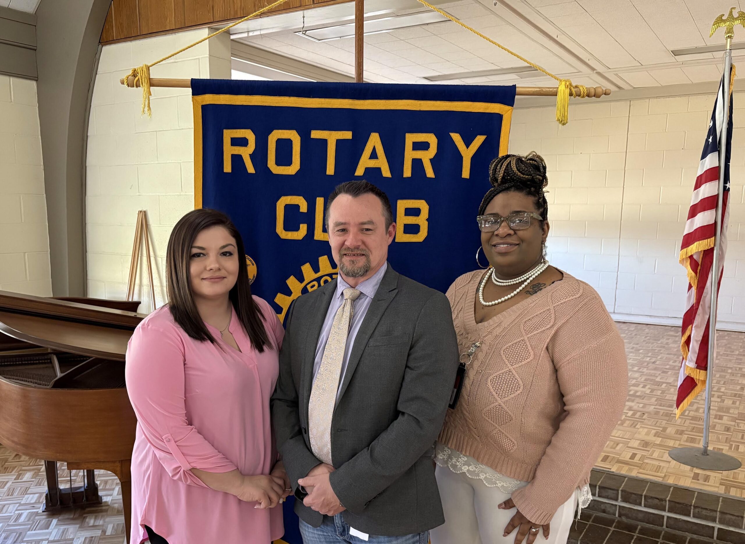 Three people standing in front of a rotary club banner.