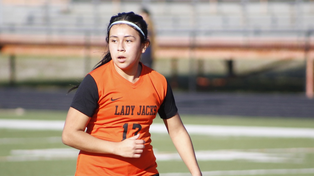 A girl in an orange and black uniform running on the field.