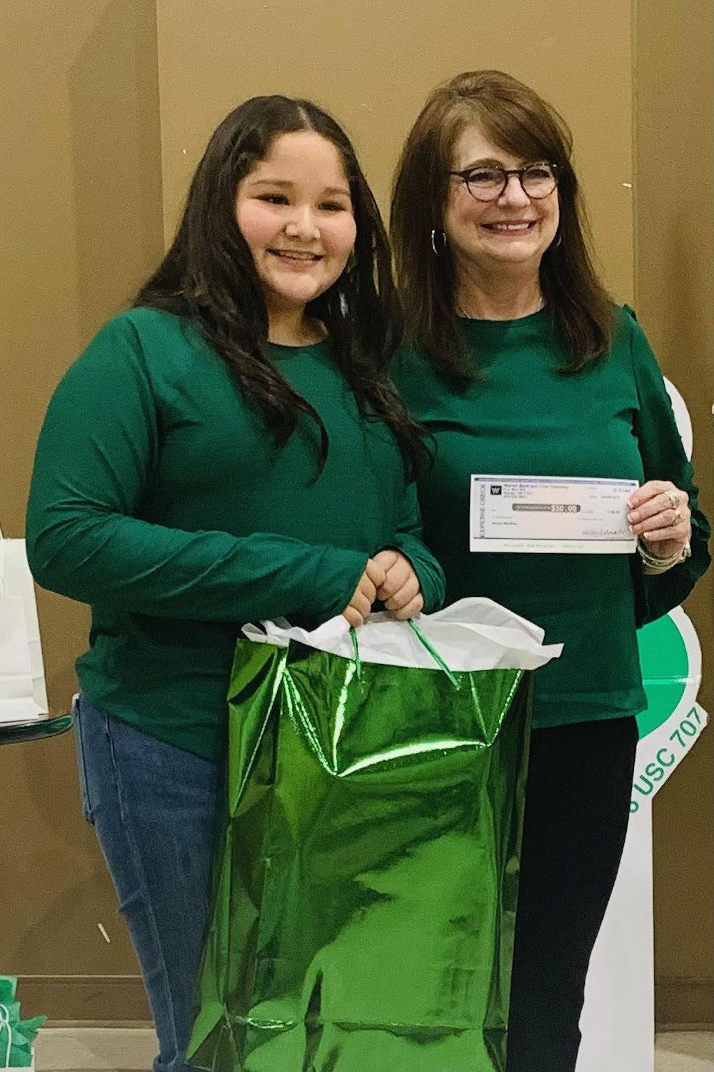 Two women holding a green bag and one is giving the other a check.