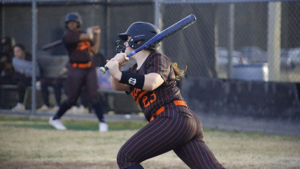 A woman in black and orange baseball uniform holding a bat.