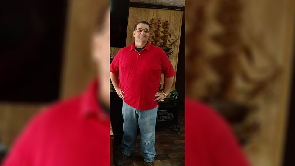 A man in red shirt standing next to a wooden wall.