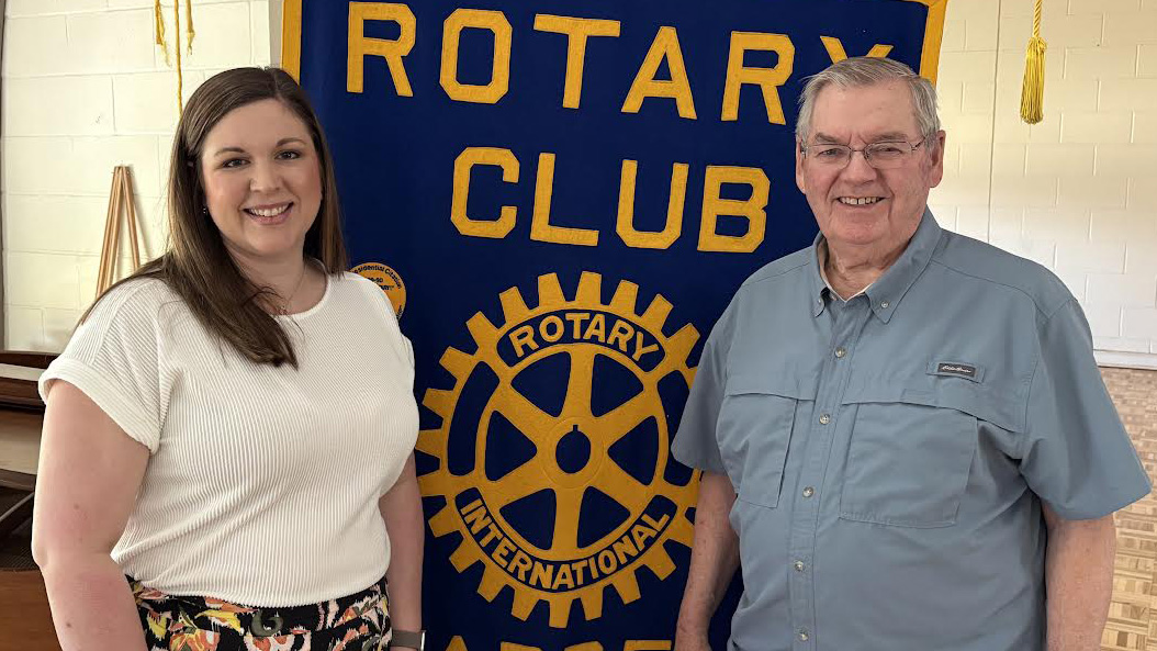 A woman and man standing in front of a rotary club banner.