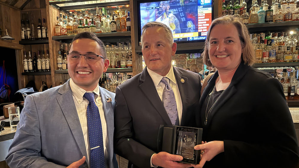 Three people in suits and ties holding a plaque.