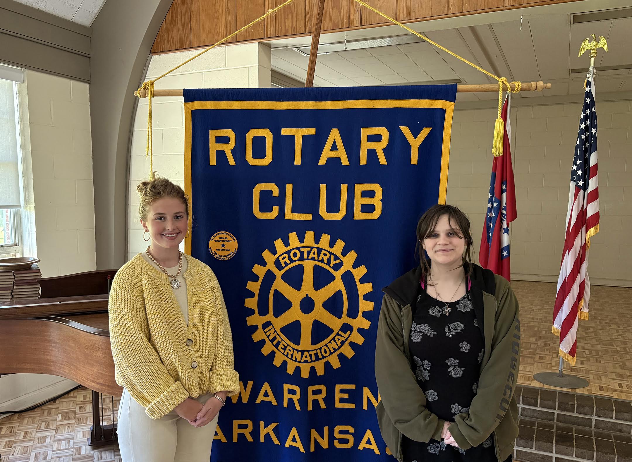 Two women standing next to a blue and yellow banner.