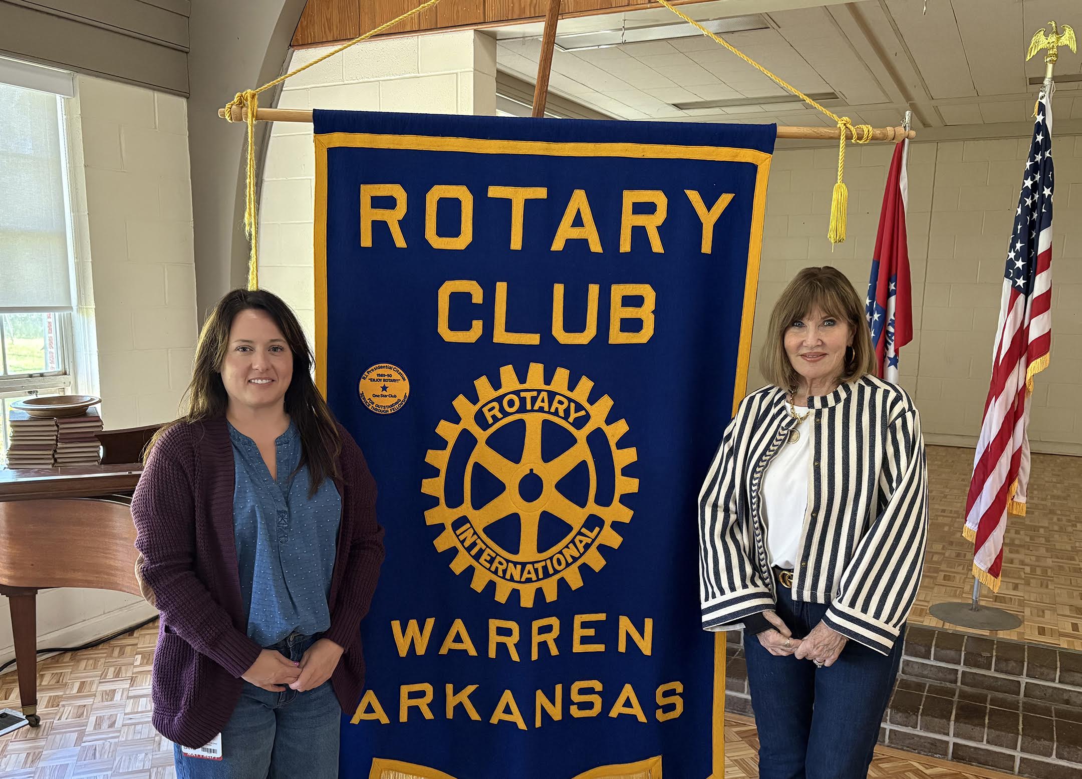 Two women standing next to a blue and yellow banner.