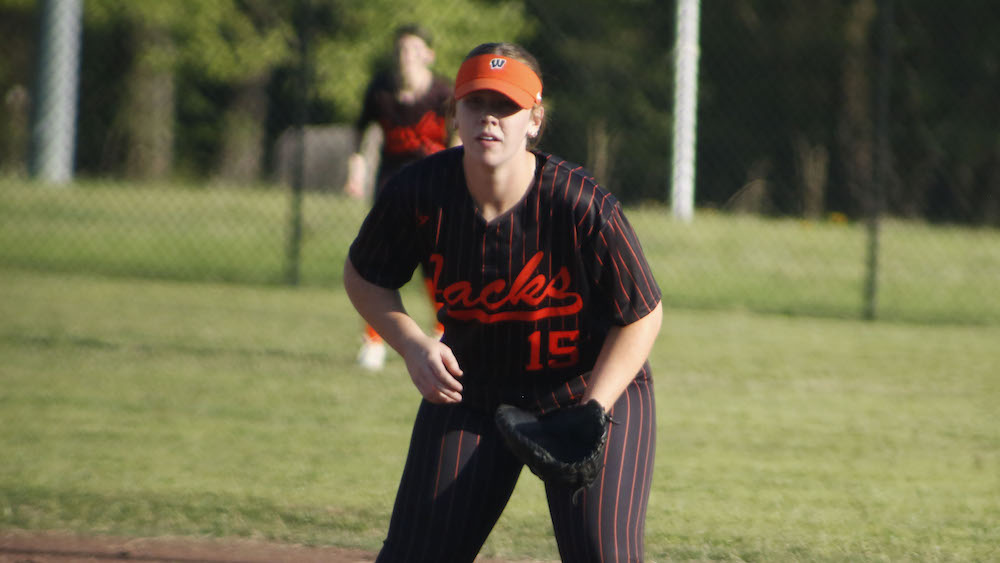 A woman in black and red baseball uniform holding a glove.