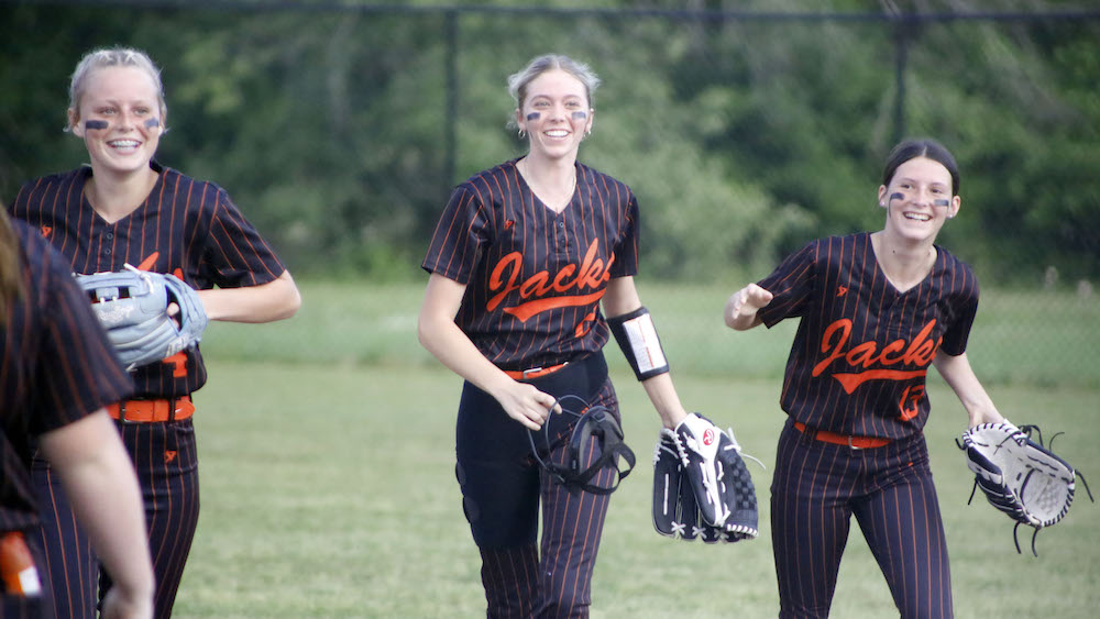 Three women in black and orange baseball uniforms.
