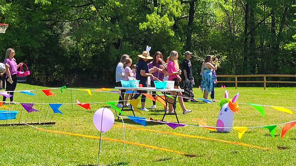 A group of people standing around a table in the grass.