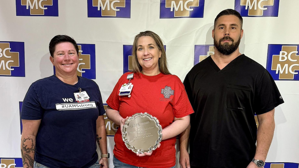Three people holding a silver platter in front of a mc sign.
