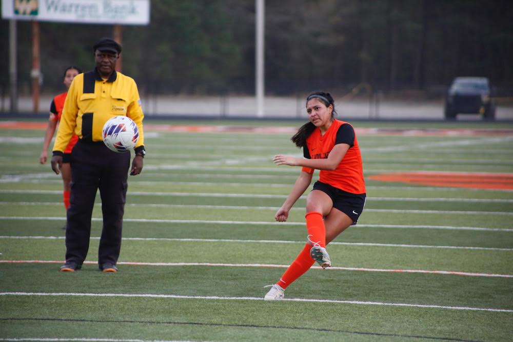 A woman kicking a soccer ball on top of a field.