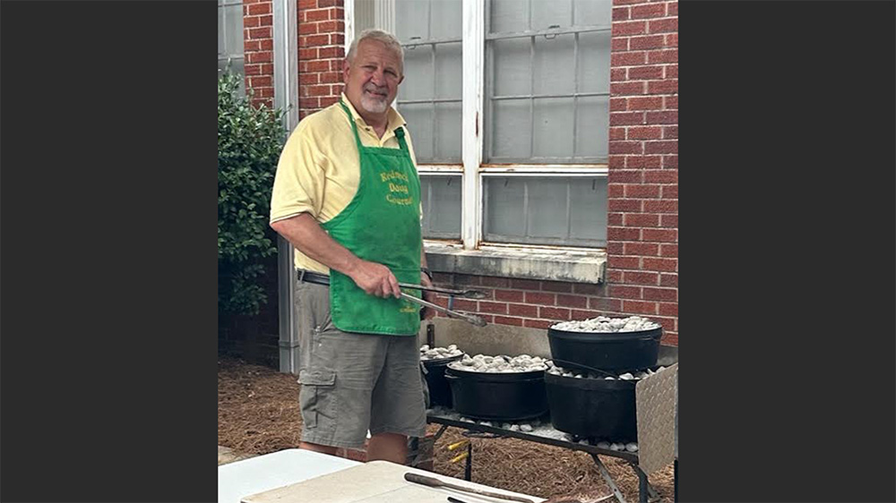 A man in an apron standing next to a grill.