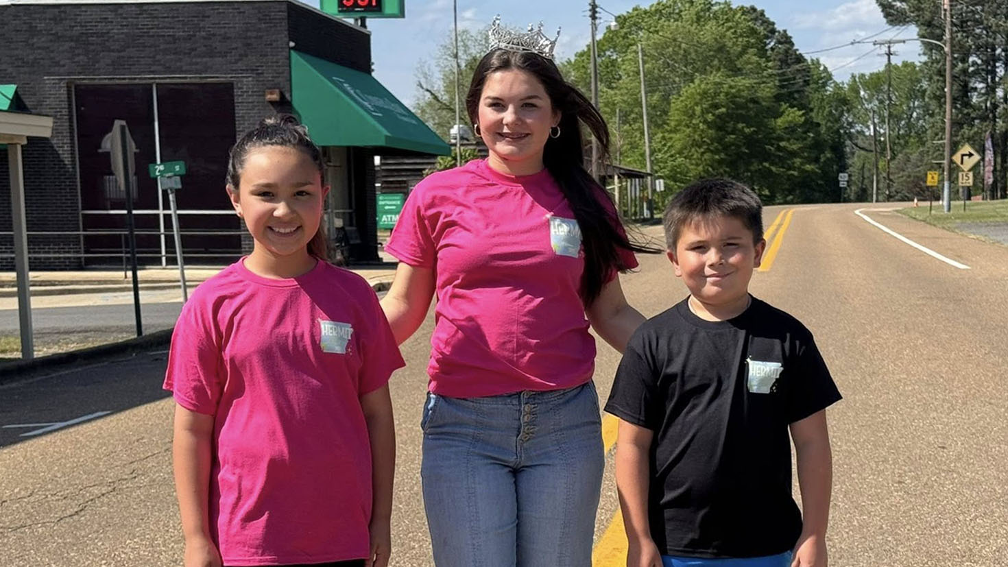 Three children standing on the side of a road.