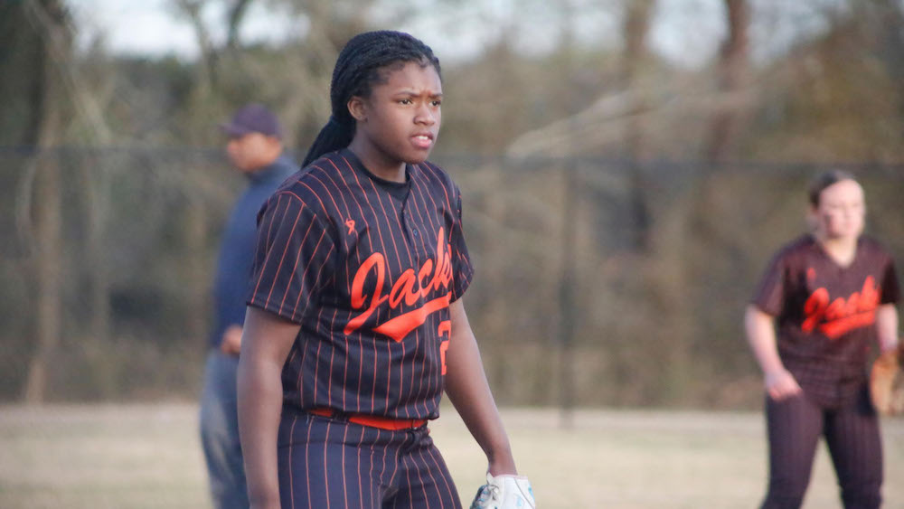 A woman in black and orange baseball uniform holding a glove.