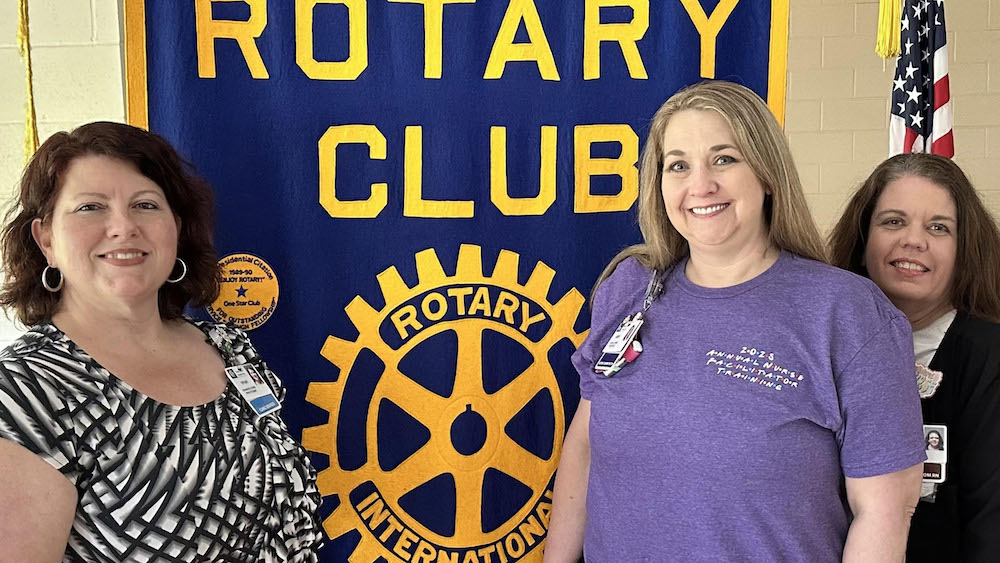 A woman standing in front of a rotary club sign.