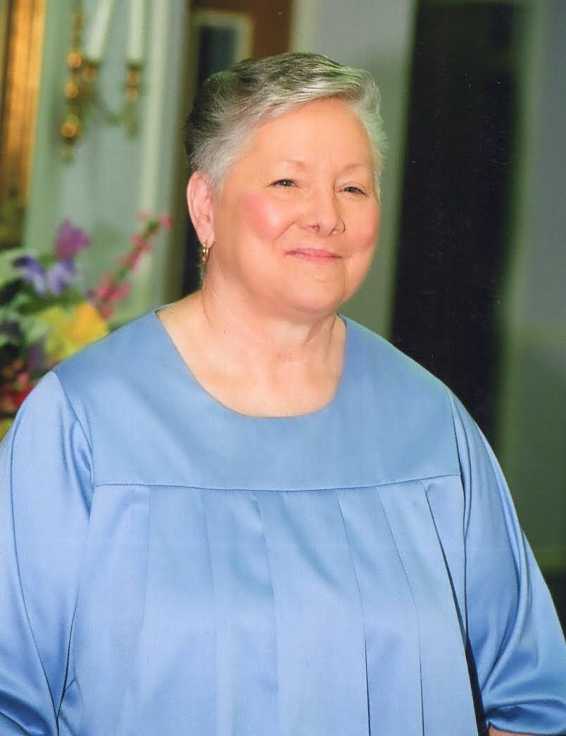 A woman in blue shirt standing next to flowers.