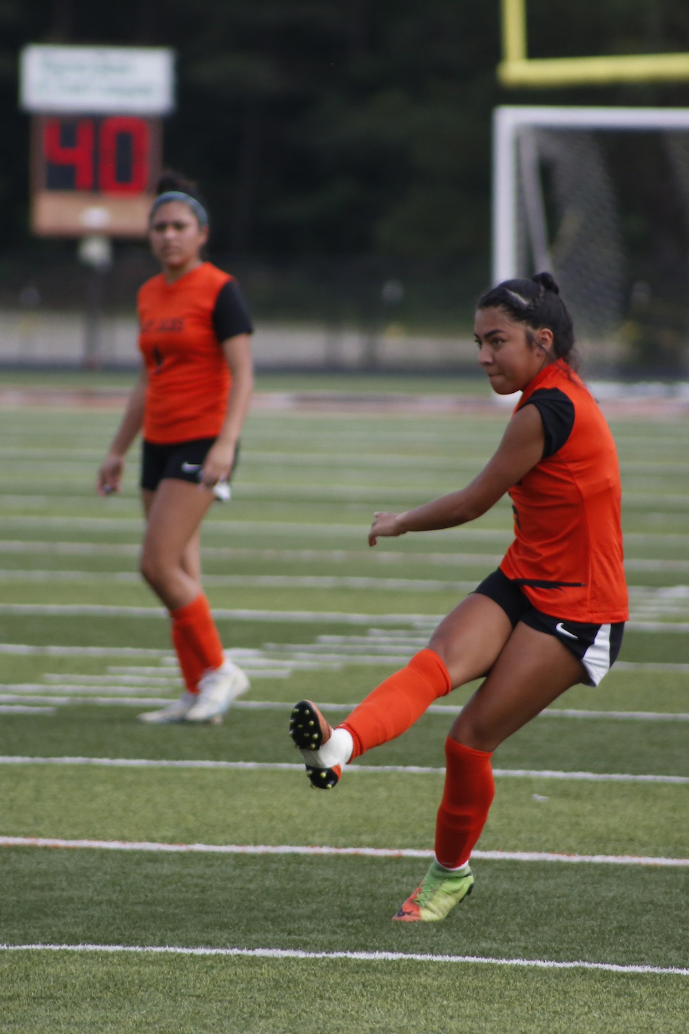 Two girls are playing soccer on a field.