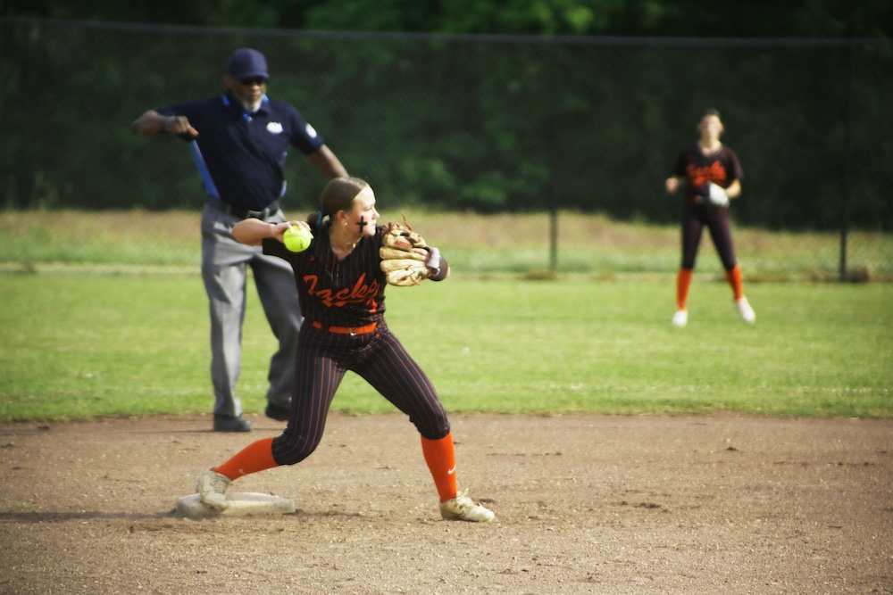 A woman in black and orange baseball uniform holding a bat.