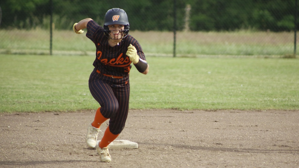 A woman in black and orange baseball uniform running.