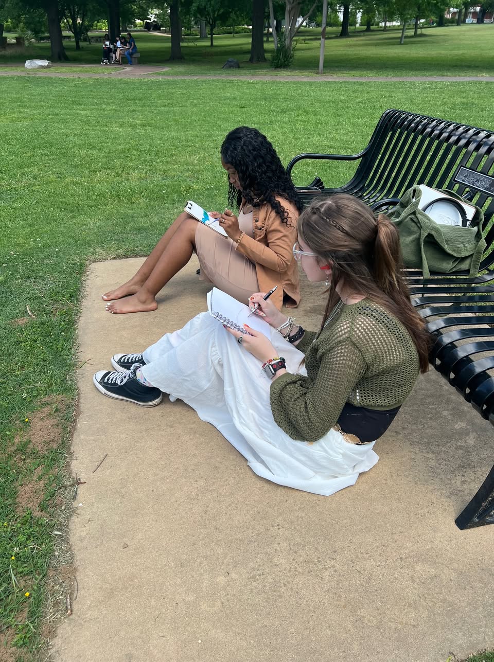 Two women sitting on a bench in the grass.