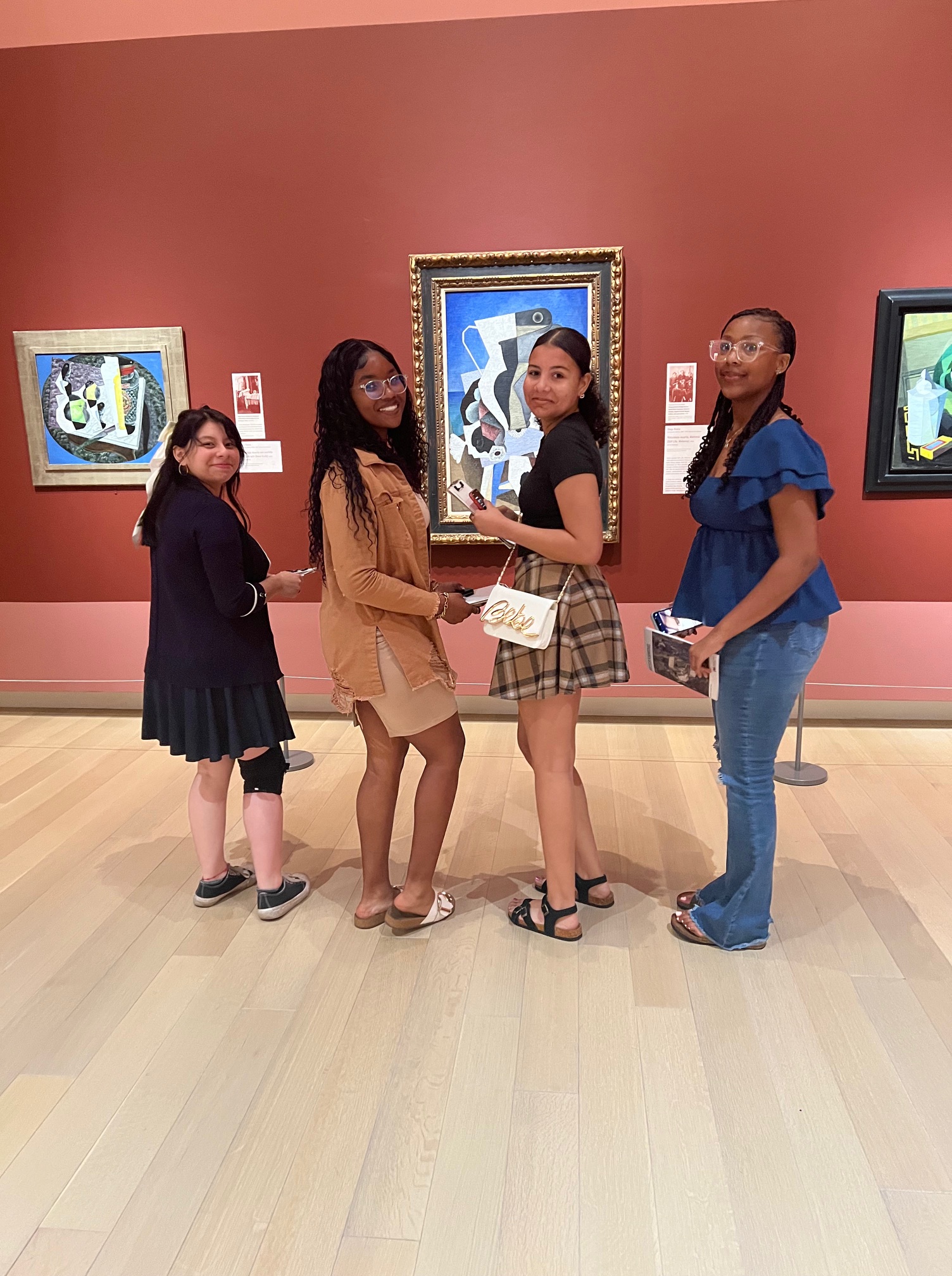 Four young women posing in front of a painting.