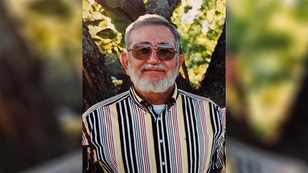 A man with white beard and sunglasses in front of a tree.